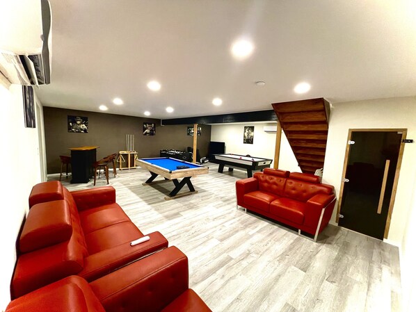 Ein Raum mit Poolbillard, roten Ledersofas, Snookertisch und einer Treppe.
