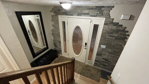 Una escalera con barandilla de madera que lleva a una habitación con pared de piedra y una puerta blanca con un panel de vidrio.