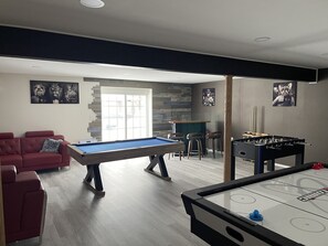 Ein modernes Wohnzimmer mit Billardtisch, Kicker und einem roten Sofa.