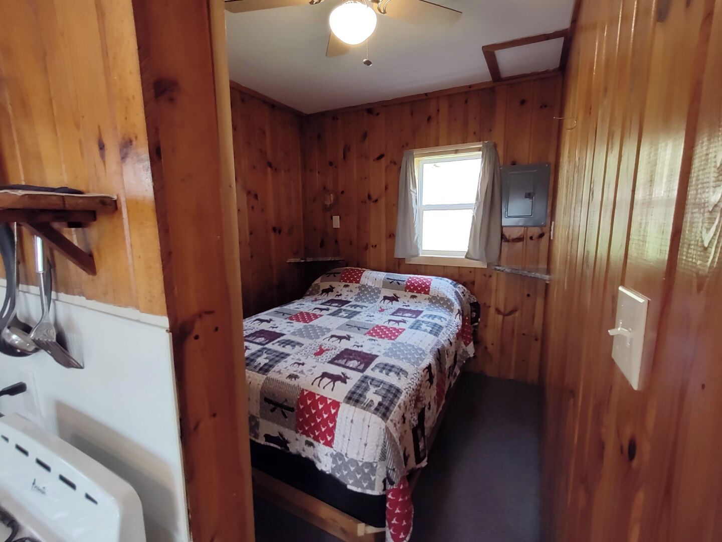 A wooden room with a bed, a window, and a ceiling fan.