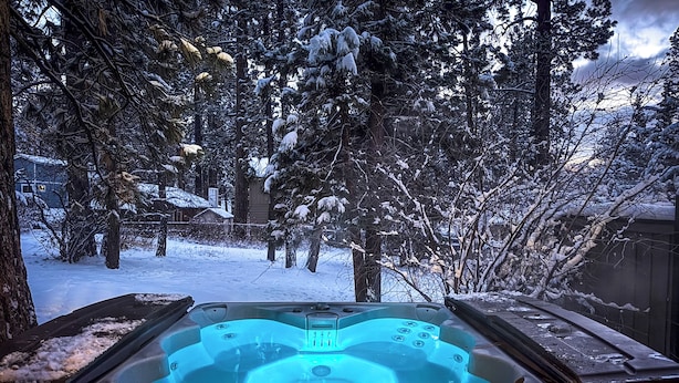 Ein Whirlpool in verschneiter Winterlandschaft mit einer Holzterrasse und umliegenden Bäumen.