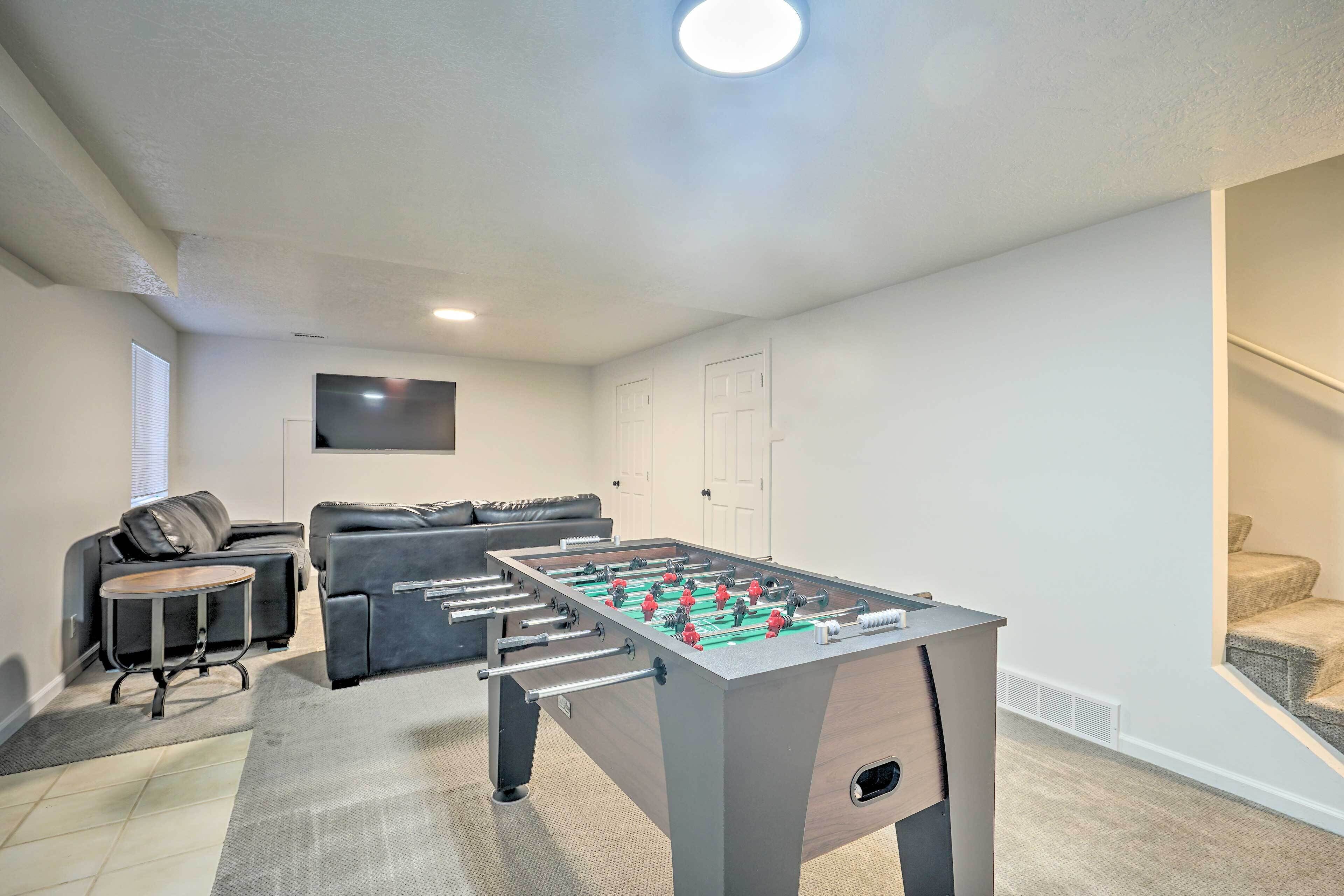 A modern living room with a foosball table, a sofa, a TV, and a staircase.