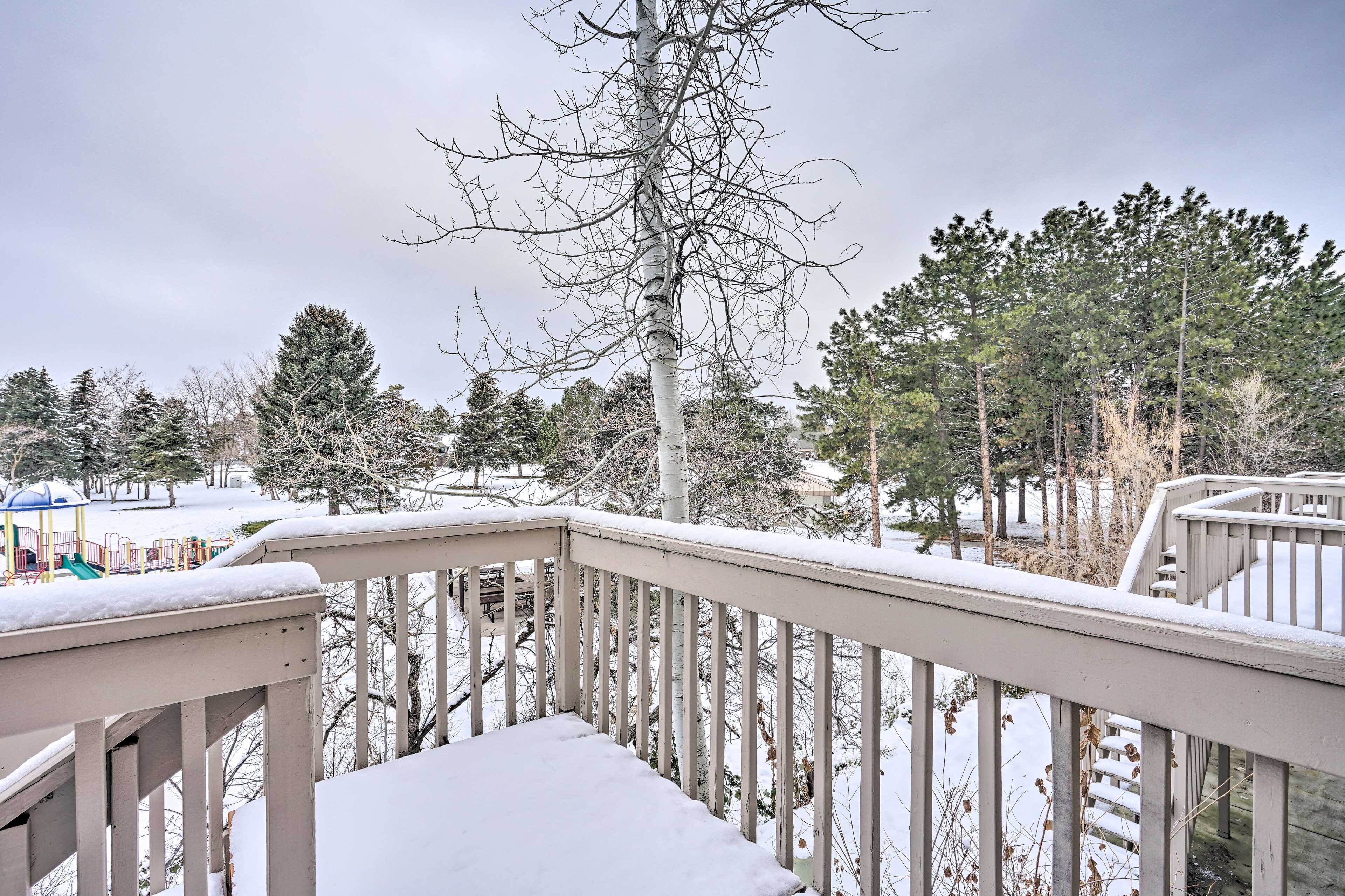 Ein mit Schnee bedeckter Balkon mit Blick auf einen Spielplatz und Bäume.