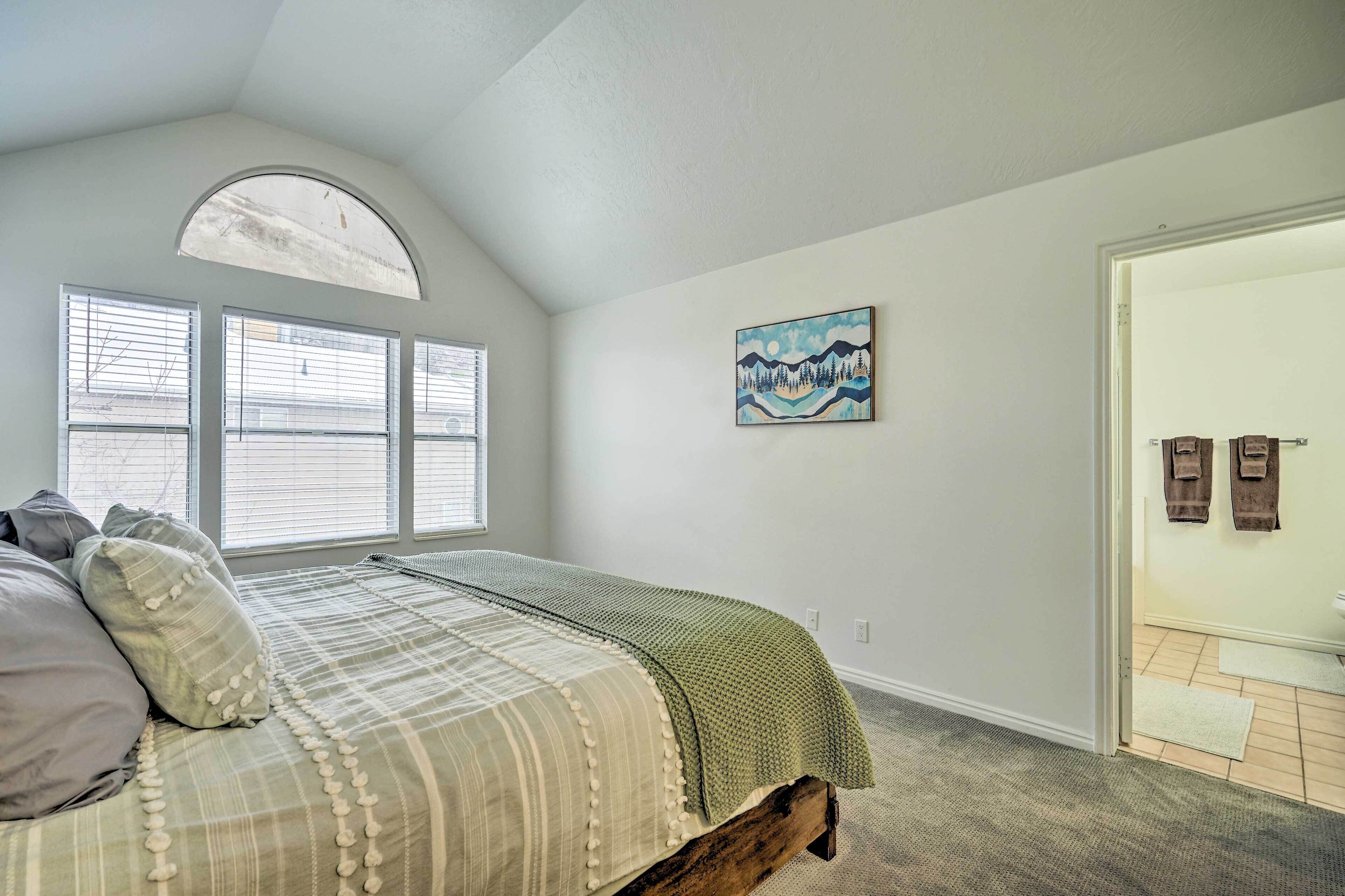 A bedroom with a bed, a window, a painting, and a door.