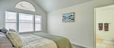A bedroom with a bed, a window, a painting, and a door.