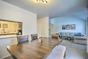 Uma sala de jantar com mesa e cadeiras de madeira, uma cozinha com pia e armários, e uma sala de estar com sofá e obras de arte na parede.
