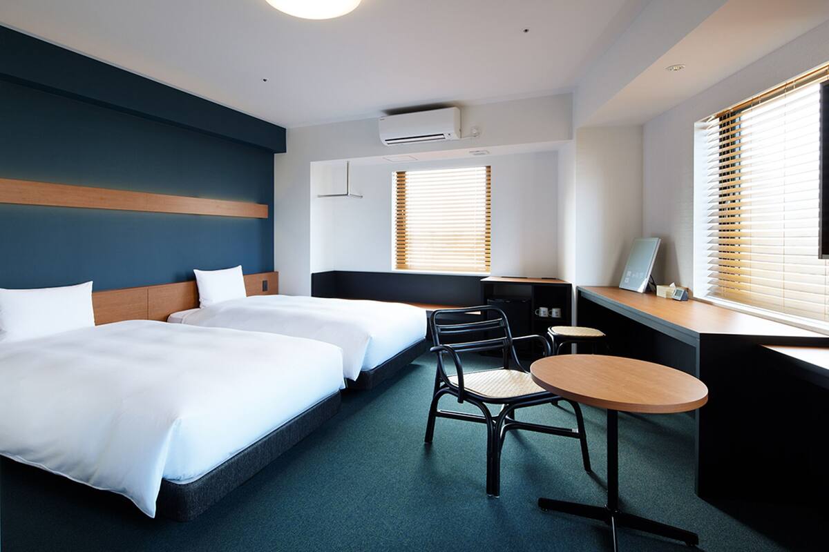 Une chambre d’hôtel avec deux lits, un bureau, une chaise et une petite table.