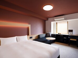 A hotel room with a large bed, a desk, a chair, a small round table, and a window with blinds. - (Naha)