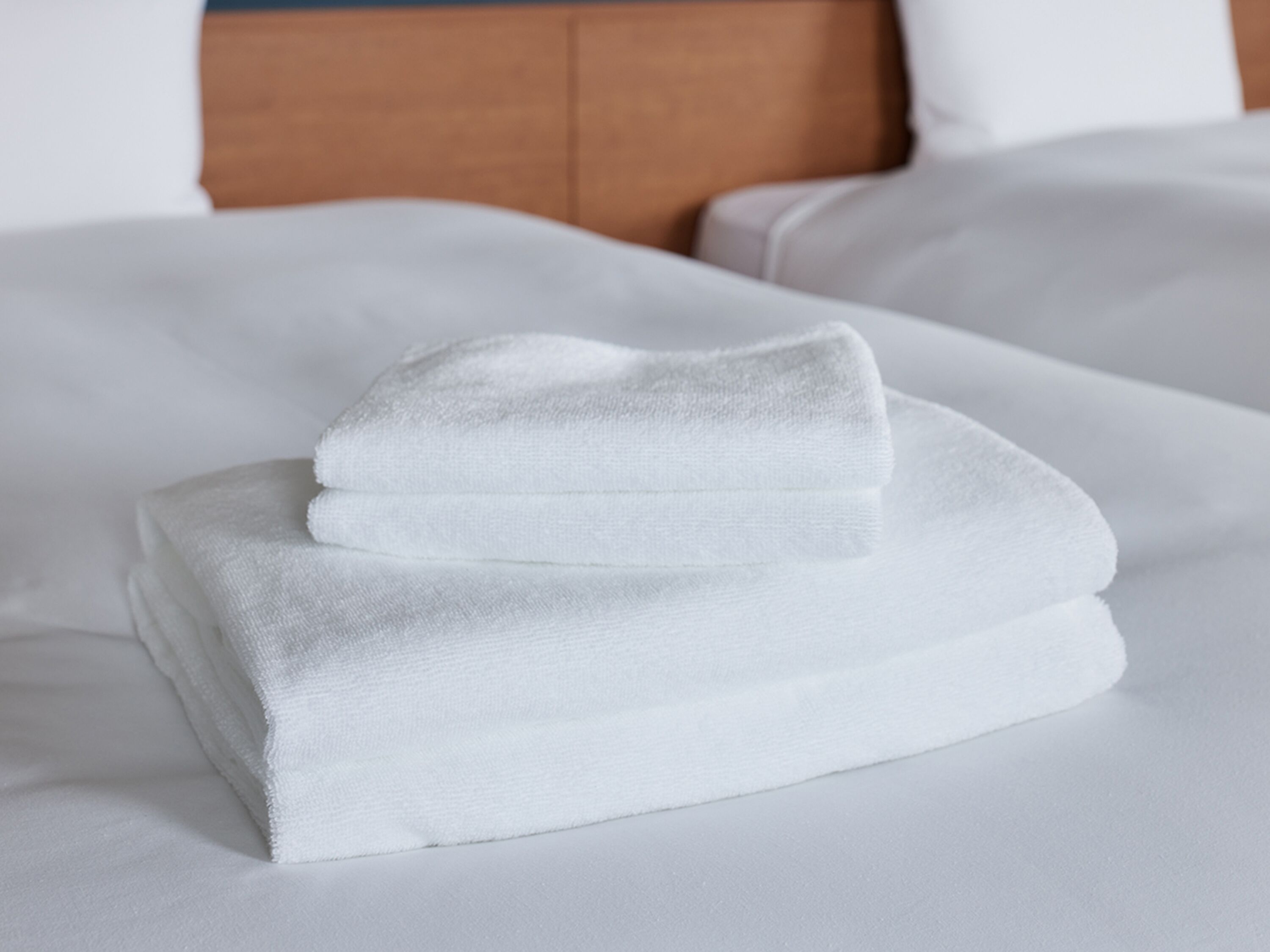 Un lit bien fait, avec du linge de lit blanc et une tête de lit en bois.