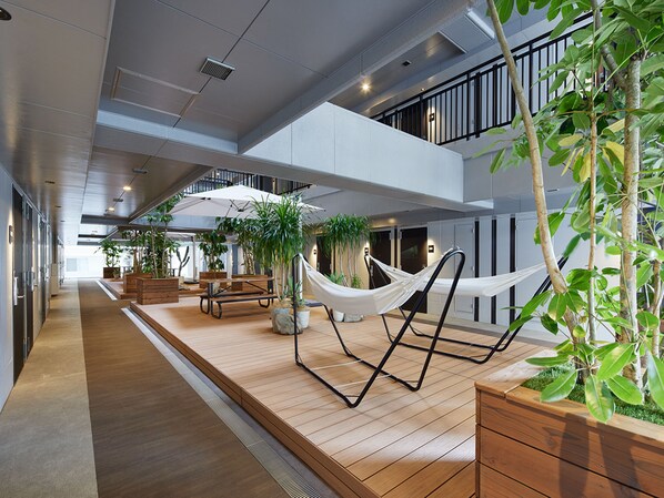 A modern indoor space with a wooden floor, a hammock, and potted plants.