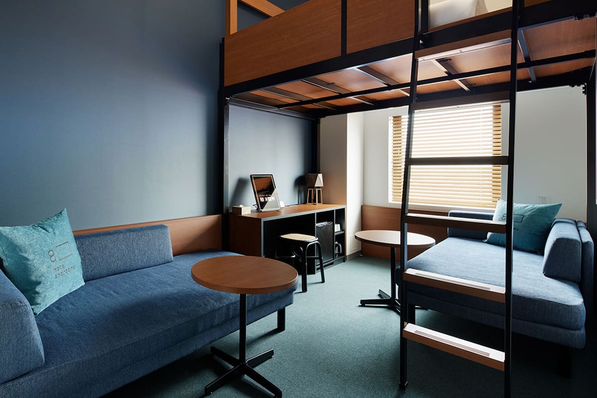 Une chambre de dortoir moderne, équipée de lits superposés, d’un canapé, d’un bureau et d’une petite table.