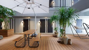 A spacious indoor area with a wooden floor, a large umbrella, and several potted plants. - hotel androoms Naha Port (Naha)