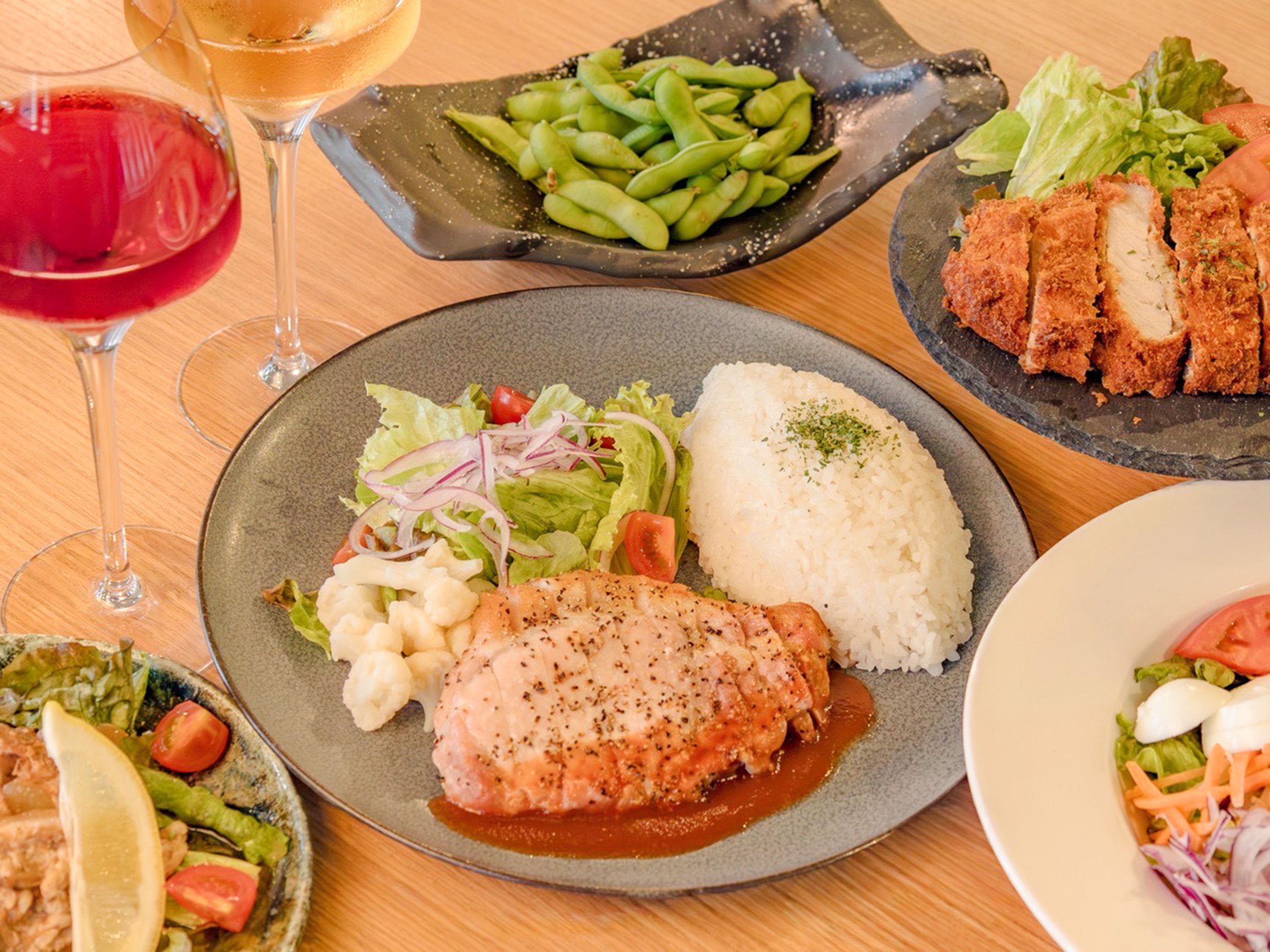 Uma mesa de jantar com diversos pratos, incluindo arroz, um filé de peixe, salada e edamame.