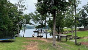 A grassy area with a trampoline, picnic table, and a dock extending into a lake. - Beautiful quiet home in cove with dock (Greenwood)