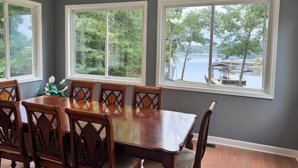 A dining room with a large table and six chairs, large windows with a view of a lake and dock, and a ceiling fan. - Beautiful quiet home in cove with dock (Greenwood)