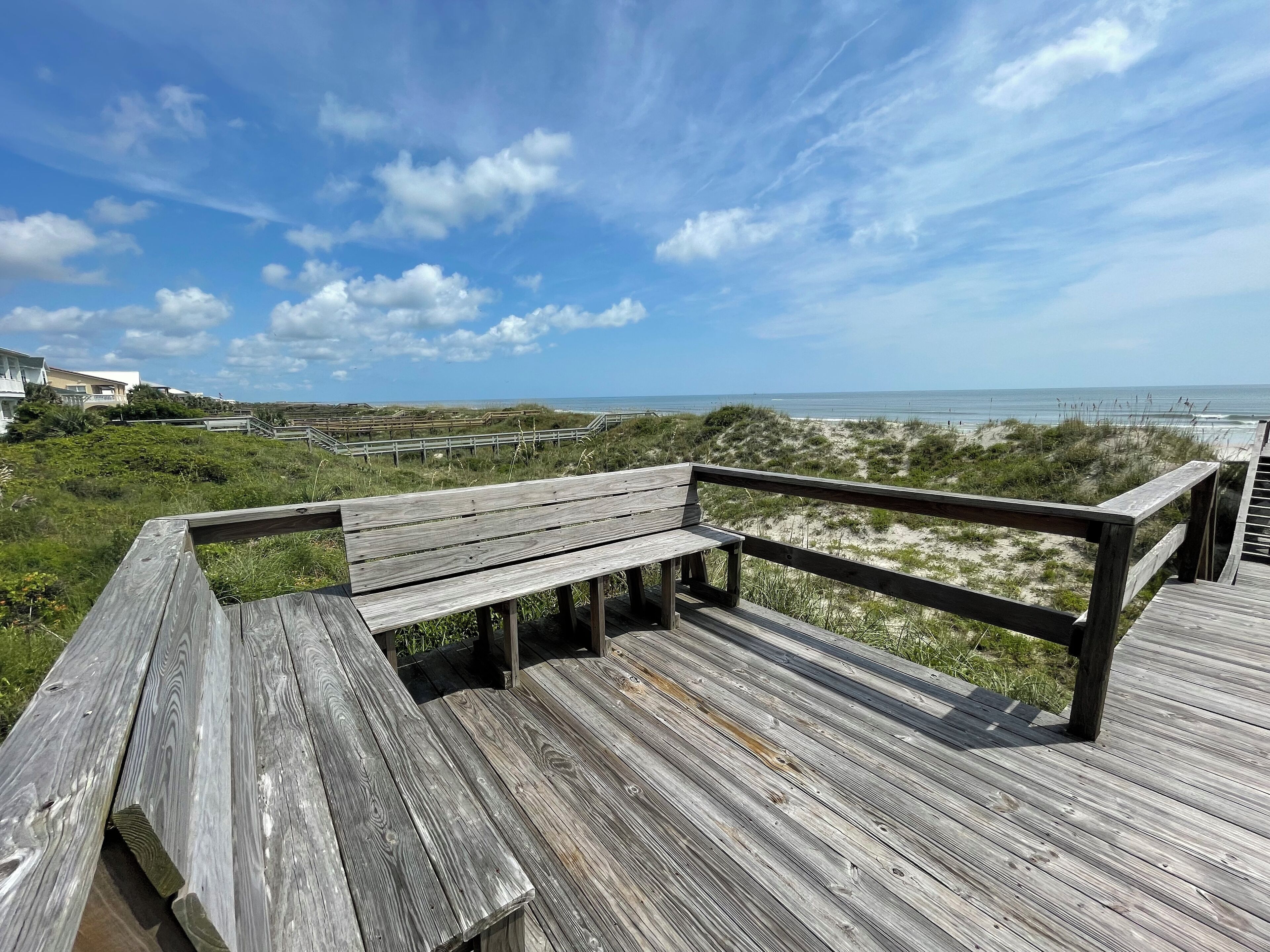 A wooden deck with benches overlooking a beach and dunes.