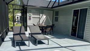 A covered outdoor area with a swimming pool, lounge chairs, and a table with chairs. - Private heated in-ground pool oasis with golf cart in Rio Grande! (The Villages)