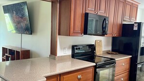 A kitchen with wooden cabinets, a microwave, a stove, and a refrigerator. - Private heated in-ground pool oasis with golf cart in Rio Grande! (The Villages)
