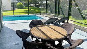 A covered outdoor area with a pool, wicker furniture, and a view of a house and greenery. - Private heated in-ground pool oasis with golf cart in Rio Grande! (The Villages)