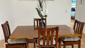 A dining area with a wooden table and chairs, a vase with white flowers, and a painting of palm trees on the wall. - Private heated in-ground pool oasis with golf cart in Rio Grande! (The Villages)