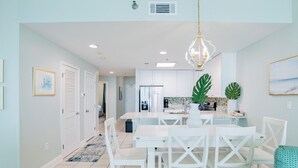 Una cocina moderna con armarios blancos, una isla central y un comedor con sillas blancas.