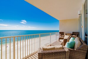 Un balcón con mobiliario de mimbre, vista a la playa y cielo despejado.