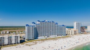 Un hotel frente a la playa con varios pisos, un área de piscina y una playa en primer plano.