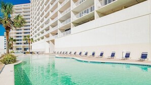 Una piscina con tumbonas y un edificio blanco con balcones.