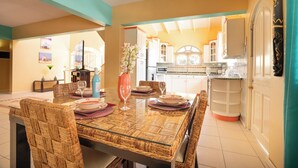 A dining area with a glass-top table, wicker chairs, and a vase of flowers.
