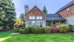 Une maison à deux étages, dotée d’un toit en pente, d’une cheminée et d’un jardin bien entretenu à l’avant, agrémenté de divers arbustes et d’une pelouse.