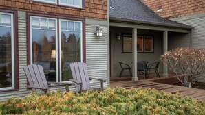 Une maison avec une véranda, deux fauteuils Adirondack et un petit jardin agrémenté de plantes à feuilles persistantes.