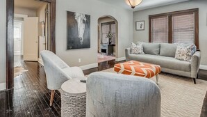 Un salon comprenant un canapé, un fauteuil, un pouf et un tableau accroché au mur.