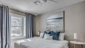 Une chambre à coucher avec un grand lit, une table de chevet, une lampe et une fenêtre avec des rideaux.
