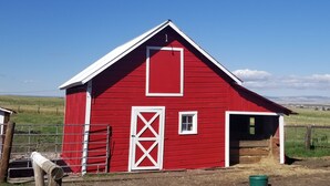 A red barn with a white door and window, surrounded by a fence and open fields. - House on the Camas Prairie - Located in Town (Grangeville)