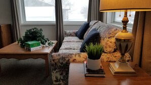 A cozy living room with a floral sofa, a small table with a plant and books, and a lamp. - House on the Camas Prairie - Located in Town (Grangeville)