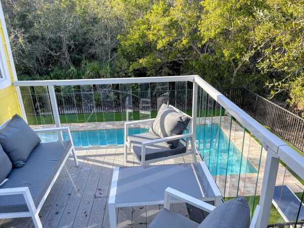 Una zona junto a la piscina con terraza blanca, piscina y área de descanso con cojines.