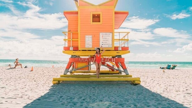 Ein Rettungsschwimmturm mit der Aufschrift "MIAMI BEACH" an einem sandigen Strand, im Hintergrund der Ozean.