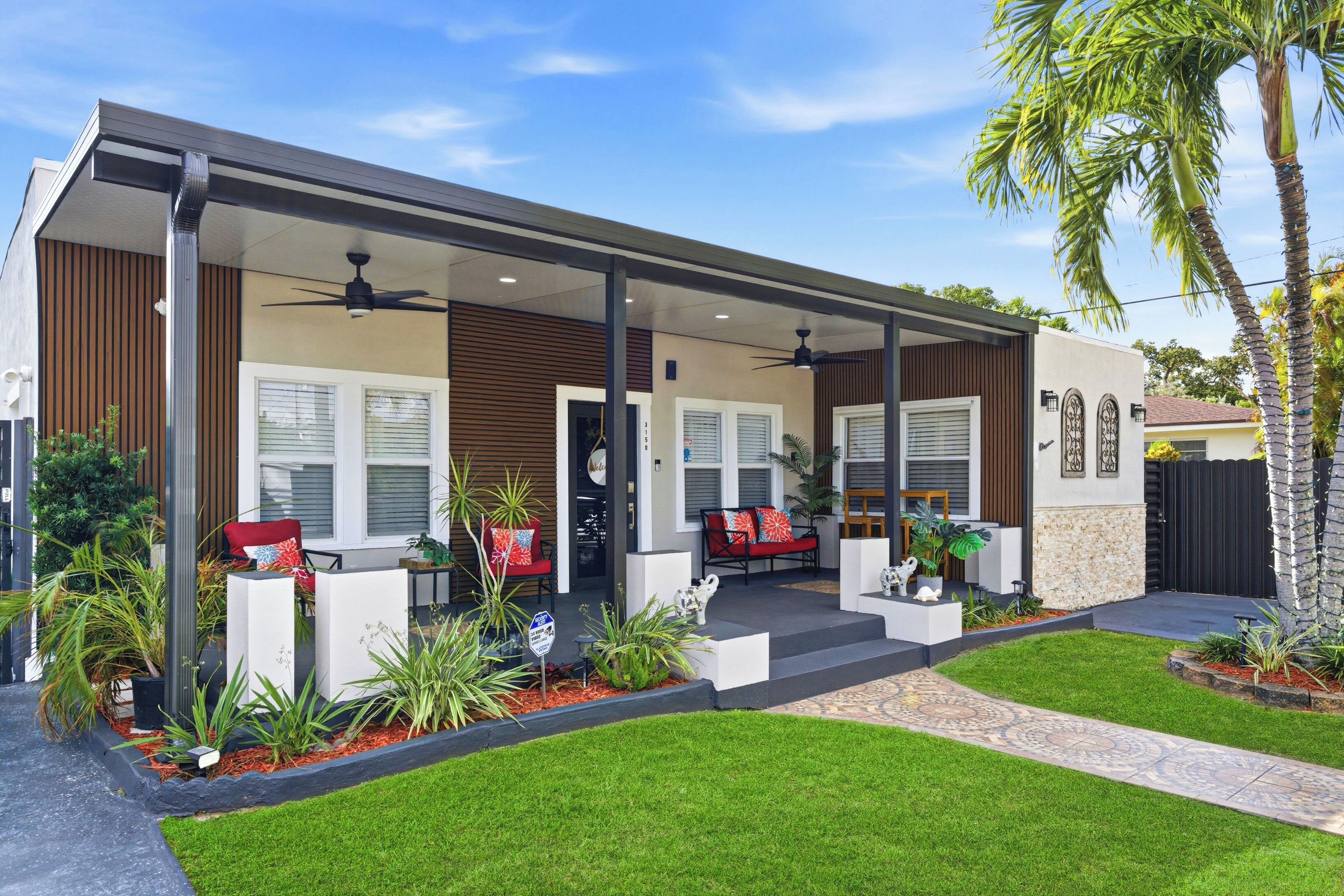Una casa moderna con un porche cubierto, mobiliario exterior y un jardín bien cuidado.
