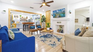 Ein modernes Wohnzimmer mit einem blauen Sofa, einem beigen Sessel und einem Essbereich mit einem Holztisch und Stühlen.