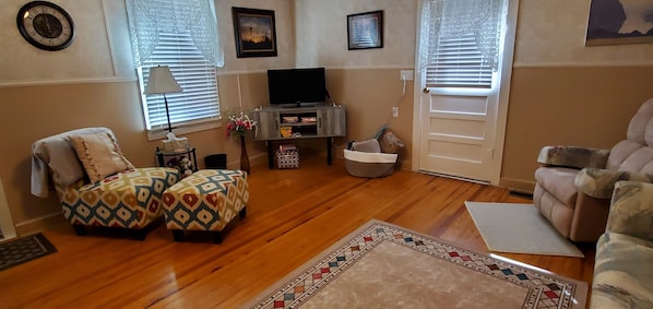 Una sala de estar con un sofá, reposapiés, televisor y una alfombra estampada.