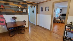 A dining area with a wooden table and chairs, a vase with flowers, and a shelf with snacks and drinks. - Make this house your HOME away from home (Meade)