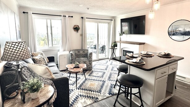 Una sala de estar moderna con sofá, sillón, mesa de centro y un comedor con taburetes y una mesa pequeña.
