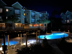 Ein Hotel bei Nacht mit Schwimmbecken, Außenbereich zum Sitzen und mehreren Balkonen.
