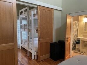 Ein Schlafzimmer mit Etagenbett, einem Holzschrank, einem Badezimmer mit Duschvorhang und einer kleinen Mülltonne.