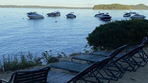 Blick auf einen See mit mehreren Booten, die im Wasser vor Anker liegen, und Liegestühlen am sandigen Ufer.