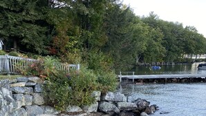 Eine Holzterrasse führt zu einer felsigen Küste, mit einem Stuhl und einem Steg, der ins Wasser ragt.
