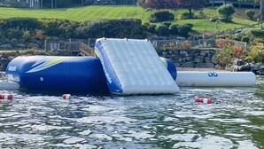 Eine Wasserrutsche in einem Gewässer, im Hintergrund Wohnhäuser.