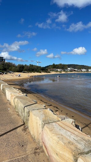 A beach with a concrete barrier, clear blue sky, and a few people in the water. - ARTNEST GETAWAY Walk to the beach - dog friendly (Ettalong Beach)
