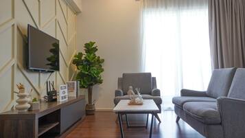 A modern living room with a flat-screen TV, a grey sofa, a coffee table, and a large plant.