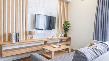 Ett modernt vardagsrum med en platt-TV som är monterad på en vägg av marmor, ett träbord med böcker och en lampa, ett soffbord och en grå soffa.